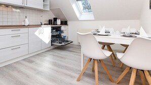 Une cuisine moderne avec des meubles blancs, un lave-vaisselle et un coin repas comprenant des chaises et une table, le tout dans des tons blancs.