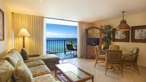 A living room with a sofa, coffee table, and wicker chairs, a television, and a large window with a view of the ocean. - Stunning Oceanviews | Aston Ka'anapali Shores 2BO2 – Pool, Hot Tub & Spa (Kaanapali)