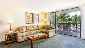 Un salón con un sofá modular, dos mesas auxiliares con lámparas y vistas a un balcón con palmeras.
