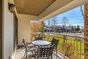 Un balcon avec une table ronde et quatre chaises, un mur en briques et une vue sur une rue bordée d’arbres et de bâtiments.