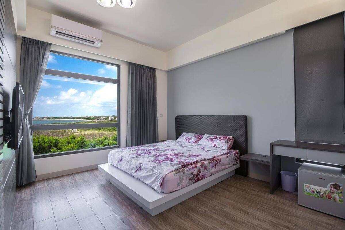 A modern bedroom with a bed, a desk, and a view of the outdoors.