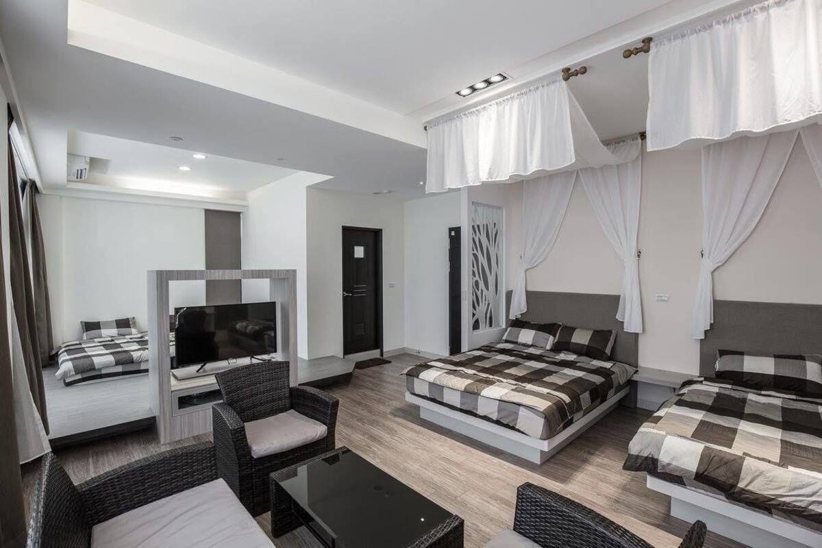 A modern hotel room with a bed, a TV, a seating area, and a balcony.