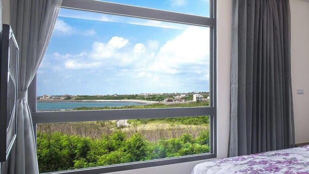 A bedroom with a large window offering a view of the sea and greenery. - 917 Homestay (Magong)