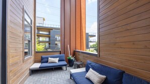 Un balcón de madera con un sofá azul y una pequeña mesa, con vistas a un edificio moderno.