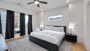 Un dormitorio moderno con una cama grande, un ventilador de techo y vistas de la ciudad a través de una ventana.