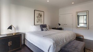 Une chambre à coucher avec un grand lit, des tables de chevet, une armoire, un tableau encadré au mur et une fenêtre donnant sur un paysage agréable.