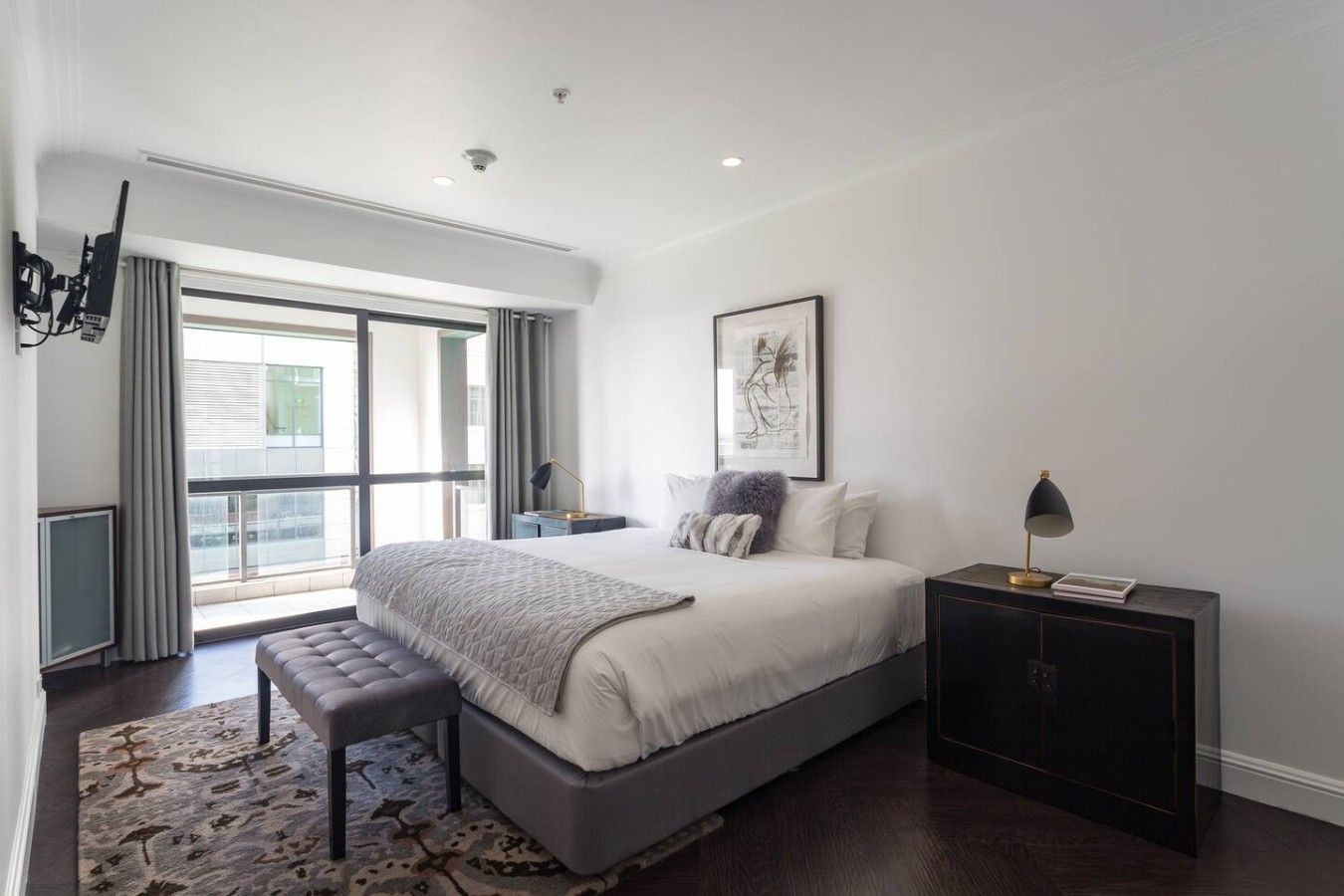 Une chambre à coucher moderne avec un grand lit, un banc, une table de chevet et une vue sur l’extérieur.