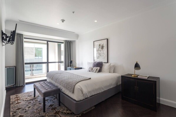 Une chambre à coucher moderne avec un grand lit, un banc, une table de chevet et une vue sur l’extérieur.