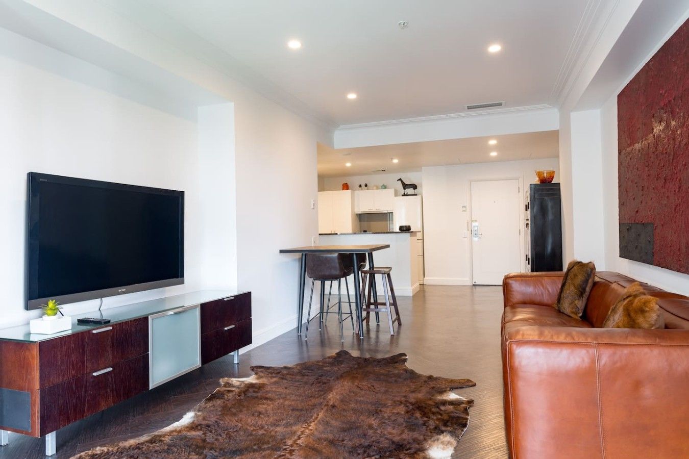 A modern living room with a leather sofa, a flat-screen TV, and a fur rug.
