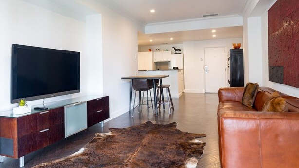 Un salon moderne avec un canapé en cuir, un téléviseur à écran plat et un tapis en fourrure.