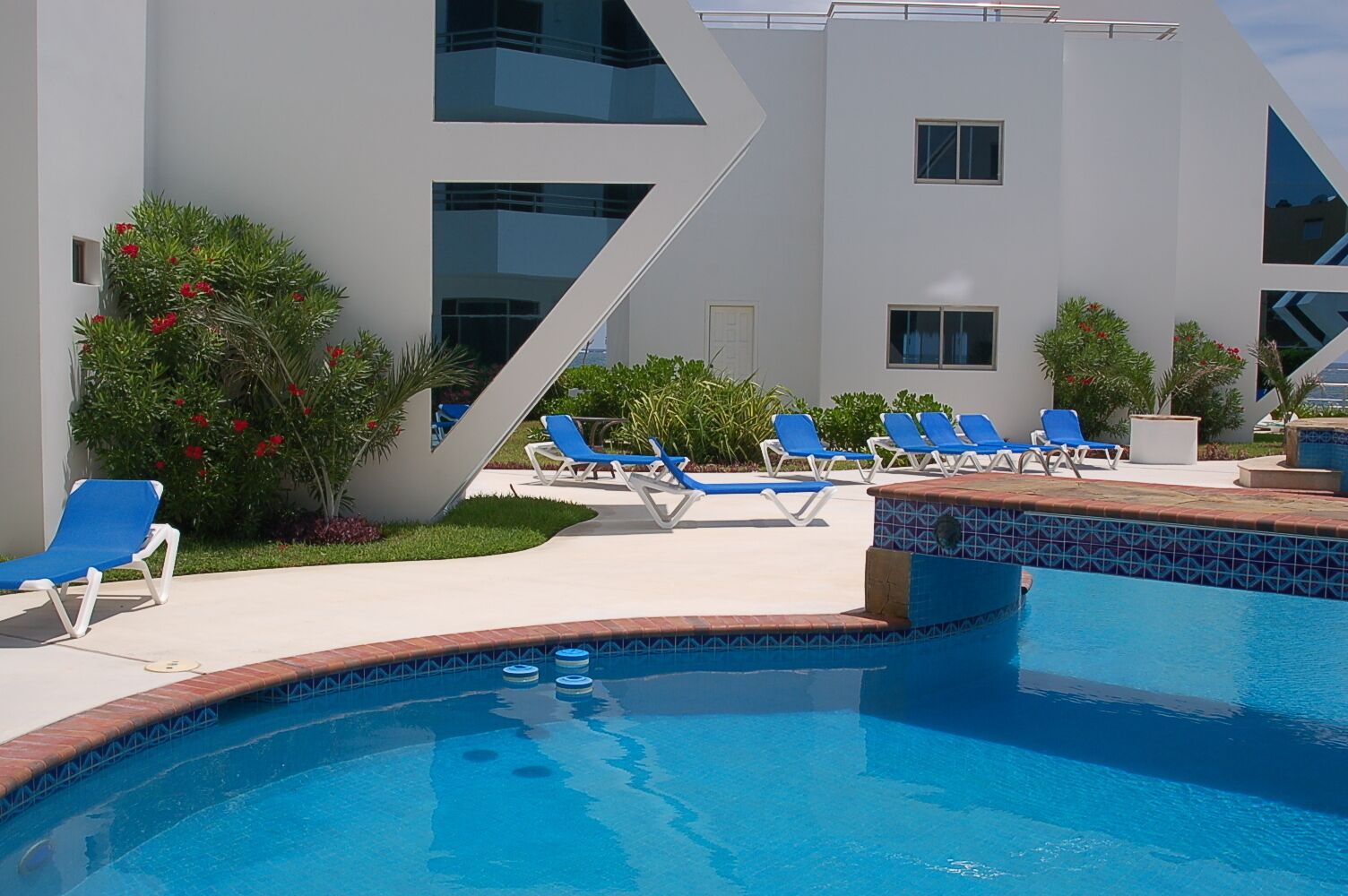 A modern pool area with blue lounge chairs and a clear blue pool.