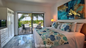 A bedroom with a bed, a television, a ceiling fan, a painting, and a view of the outdoors. - Oceanfront Luxury Townhome Condo Wifi 3 Smart TV'S Pool & Spa (Puerto Morelos)