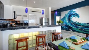 A modern kitchen with a central island, bar stools, and a dining area with a table set for two. - Oceanfront Luxury Townhome Condo Wifi 3 Smart TV'S Pool & Spa (Puerto Morelos)