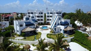 A modern resort with multiple white buildings, a central swimming pool, and surrounding palm trees. - Oceanfront Luxury Townhome Condo Wifi 3 Smart TV'S Pool & Spa (Puerto Morelos)