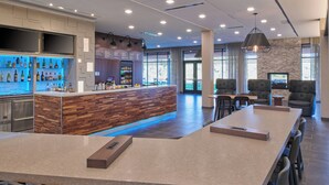 A modern bar area with a wooden counter, seating with high backs, and a stone accent wall. - Courtyard by Marriott Petoskey at Victories Square (Petoskey)