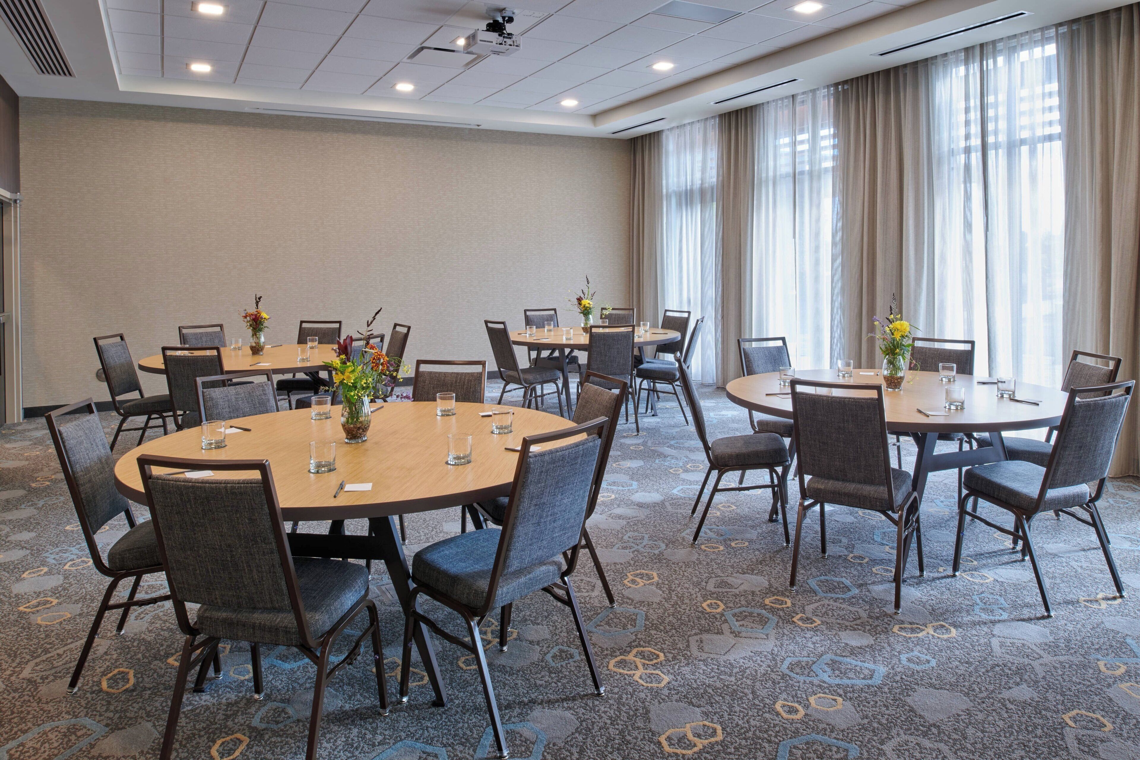 A conference room with multiple round tables, each with chairs and small vases with flowers.