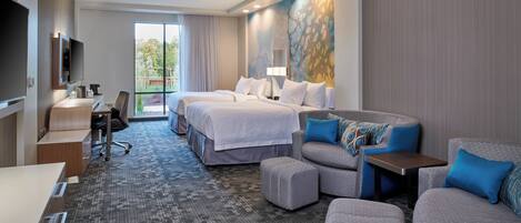 A hotel room with a large bed, two smaller beds, a sofa, a desk, and a TV.