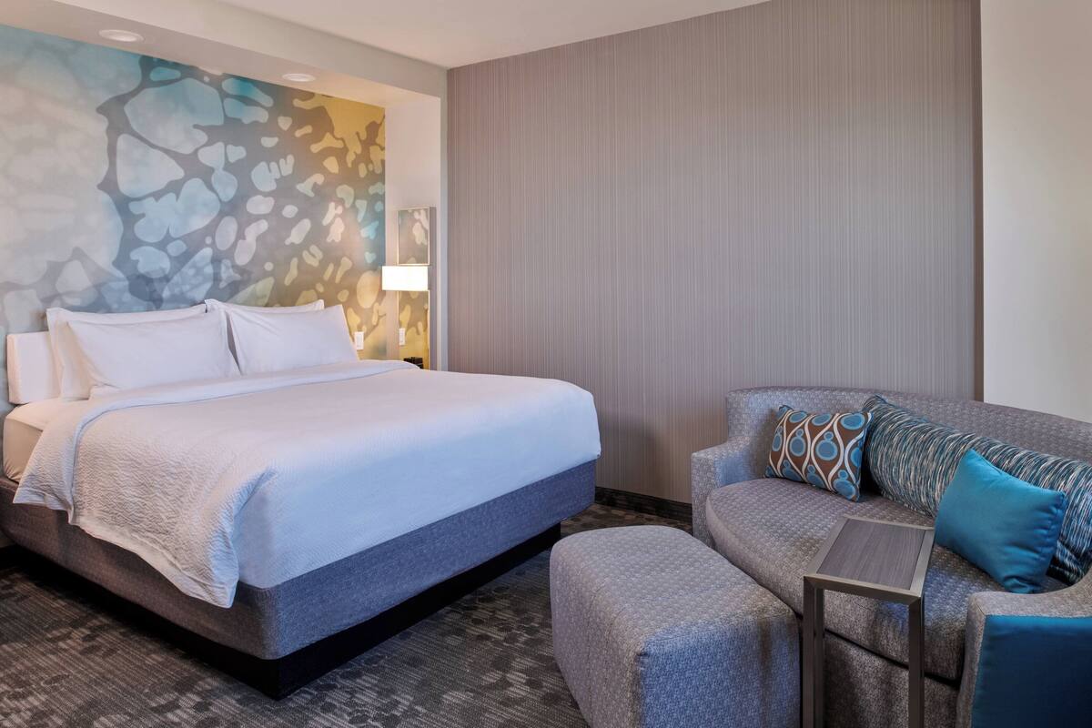 A hotel room with a bed, a sofa, a small table, and a wall with abstract art.