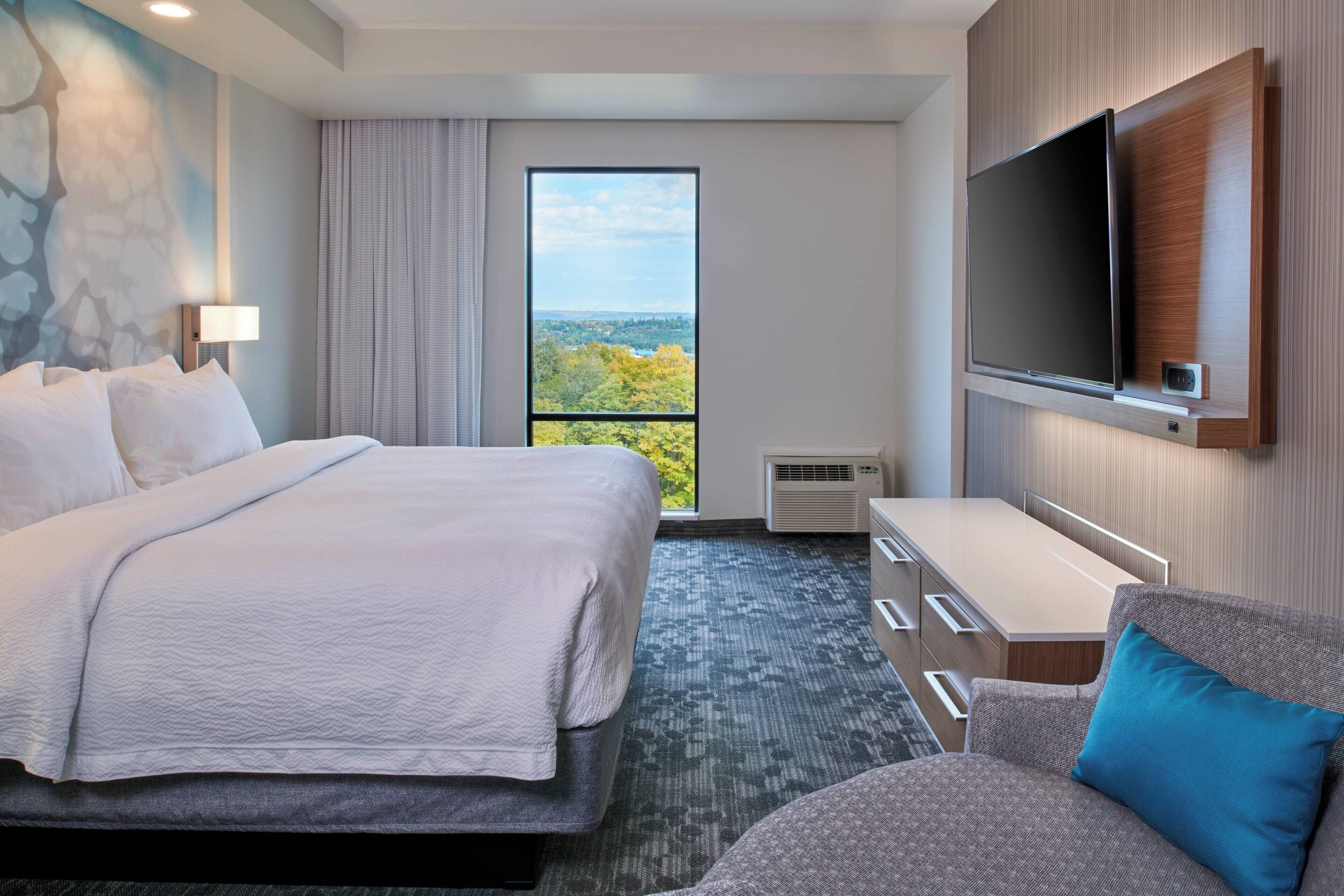 Une chambre d’hôtel dotée d’un grand lit, d’un téléviseur à écran plat fixé au mur, d’un bureau et offrant une vue sur l’extérieur par une fenêtre.
