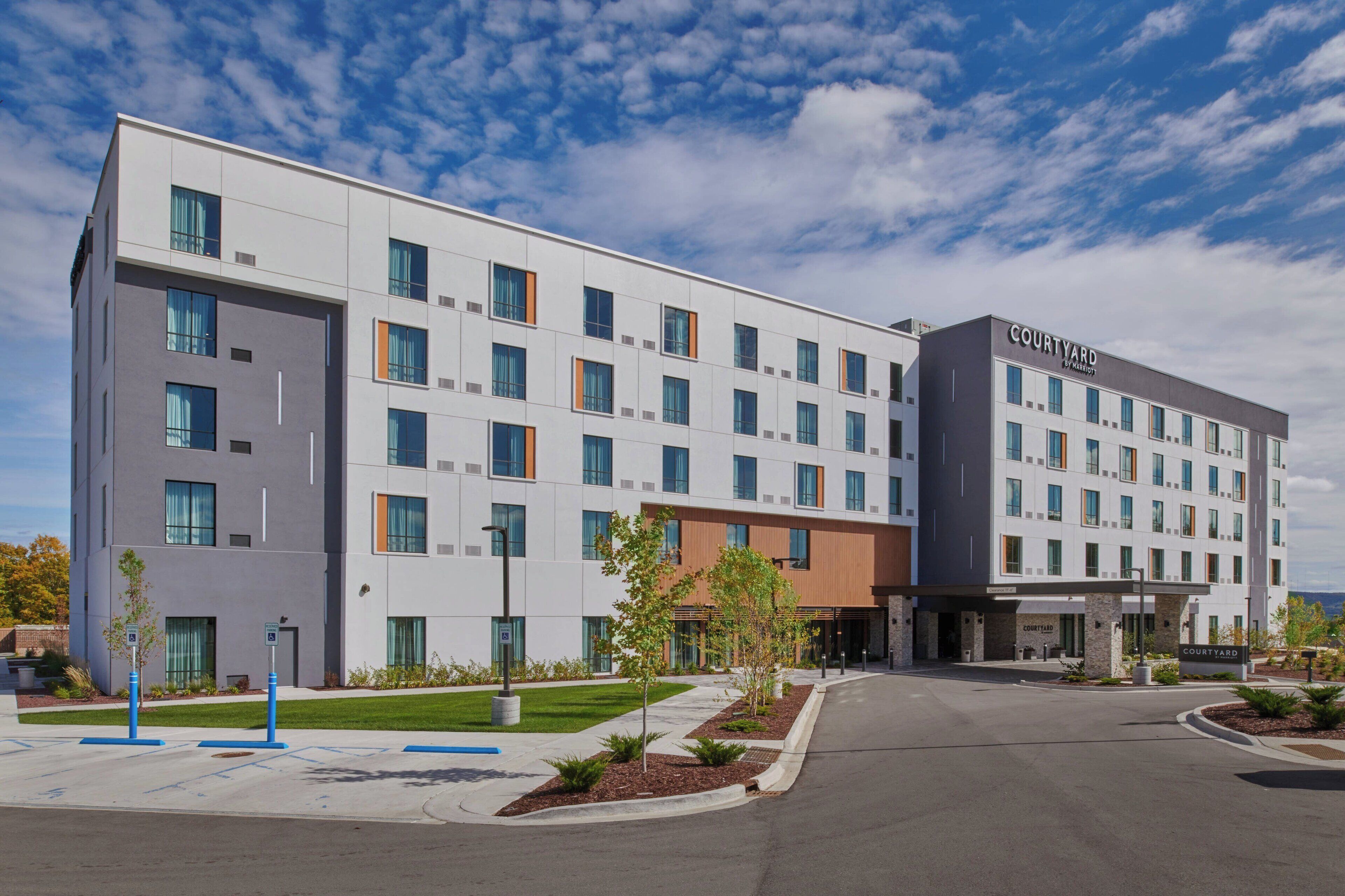 A Courtyard hotel with a modern design, featuring a mix of white and gray exterior walls, multiple windows, and a landscaped entrance area.