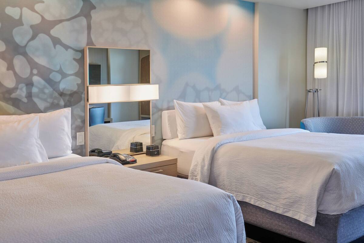 A hotel room with two beds, a bedside table with a lamp, a mirror, and a wall with a textured design.