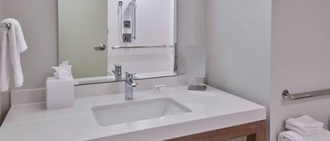 A modern bathroom with a white sink, a mirror, a towel rack, and a shower area.