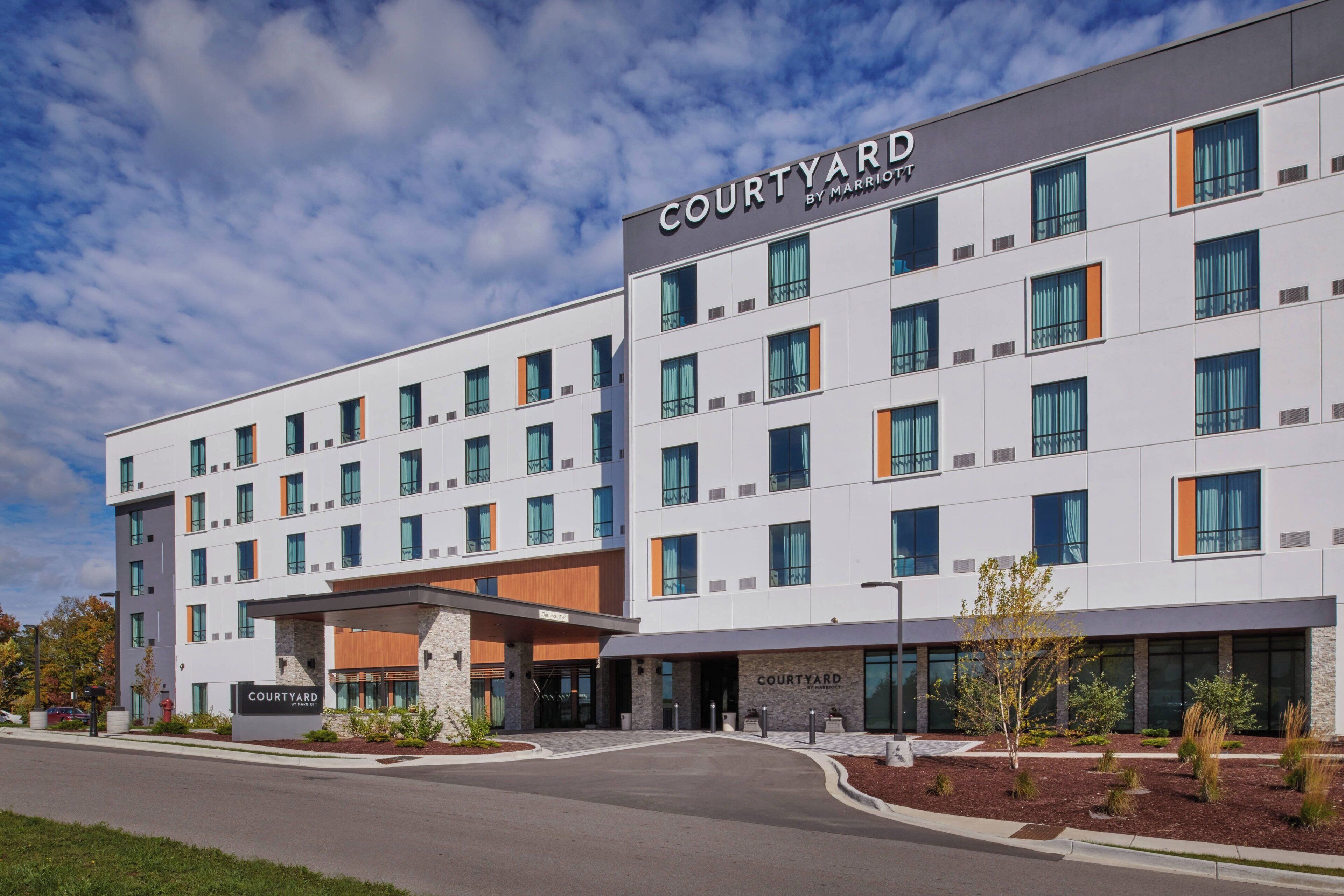 Un hôtel Courtyard by Marriott au design moderne, caractérisé par une façade plate, de nombreuses fenêtres et un espace d’entrée aménagé.