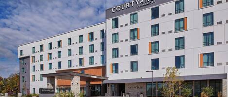 Hotel Courtyard by Marriott dal design moderno, con facciata lineare, numerose finestre e area d'ingresso curata con giardini.
