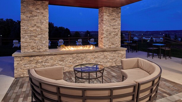 An outdoor patio with a stone fireplace, cushioned seating, and a view of the landscape. - Courtyard by Marriott Petoskey at Victories Square (Petoskey)