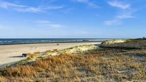 Ein Strand mit sandigem Ufer, Holzbarrieren und blauem Himmel.