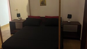 Een slaapkamer met hemelbed, twee nachtkastjes met lampen, een poster aan de muur en een betegelde vloer.