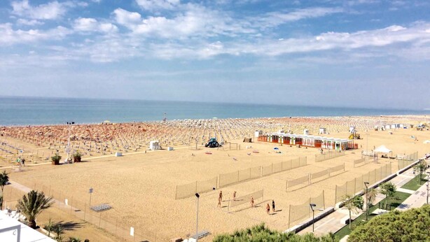 Une plage avec un terrain de volley-ball, des parasols et des cabanes de plage.