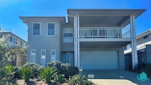 A two-story residential building with a garage, a balcony on the upper floor, and a small garden area with plants. - The Sanctuary By The Sea – family and Pet Friendly, walk to the Beach (Catherine Hill Bay)