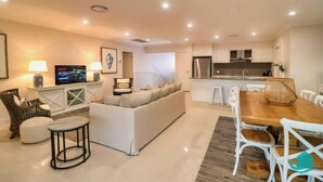A modern living room with a sofa, a wooden dining table, and a TV. - The Sanctuary By The Sea – family and Pet Friendly, walk to the Beach (Catherine Hill Bay)