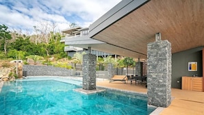 A modern pool area with a clear blue pool, stone pillars, and a wooden deck. - Hidden Cove 6, Stunning Seaview Apartment on Hamilton Island (Hamilton Island)