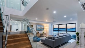 A modern living room with a grey sofa, wooden staircase, and a large window overlooking the sea. - Hidden Cove 6, Stunning Seaview Apartment on Hamilton Island (Hamilton Island)
