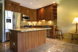 A kitchen with wooden cabinets, stainless steel appliances, granite countertops, and a bar stool.