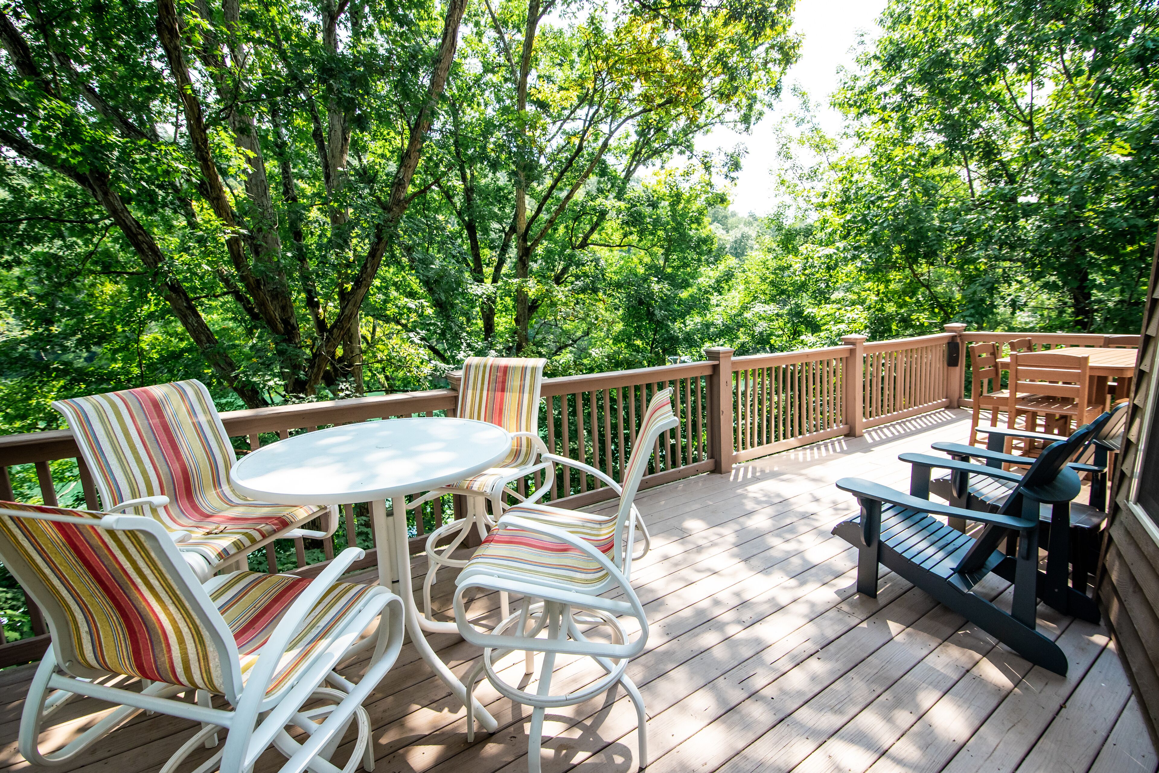 Une terrasse en bois, agréée de mobilier d’extérieur, notamment des chaises et une table, et entourée d’une végétation luxuriante.