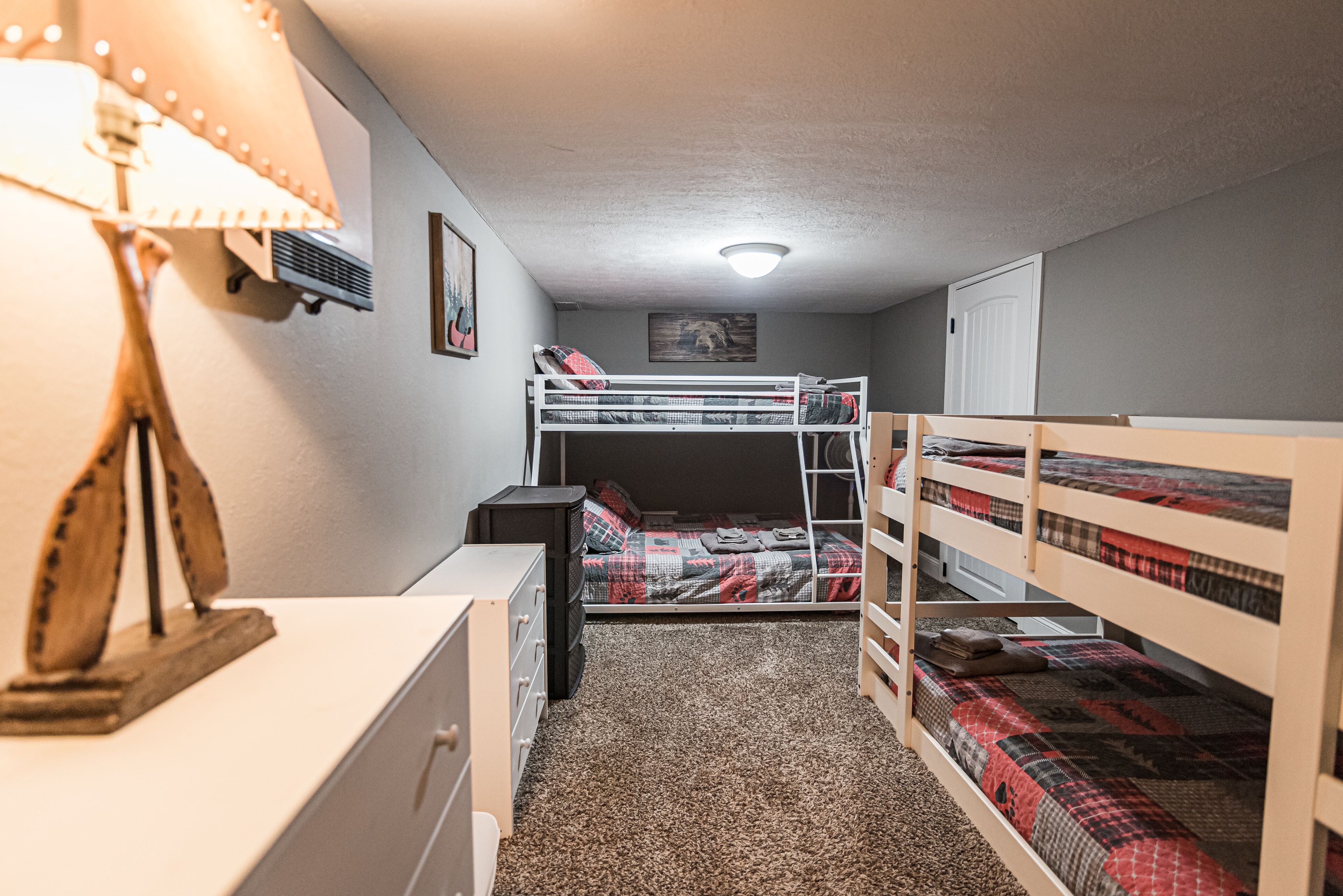 Una habitación pequeña con literas, escritorio, lámpara y cómoda.