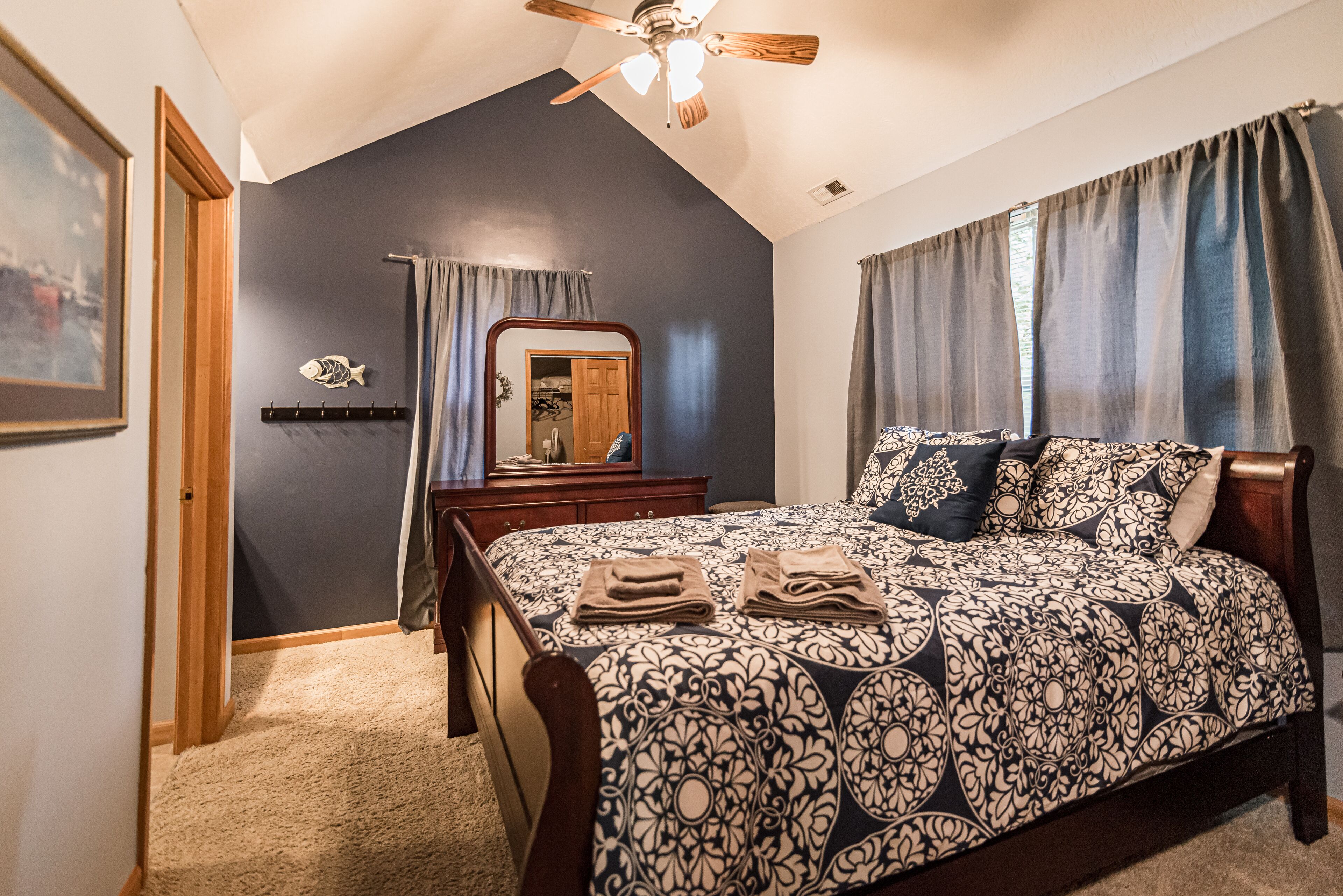 A bedroom with a bed, a ceiling fan, a dresser, a mirror, and a door.