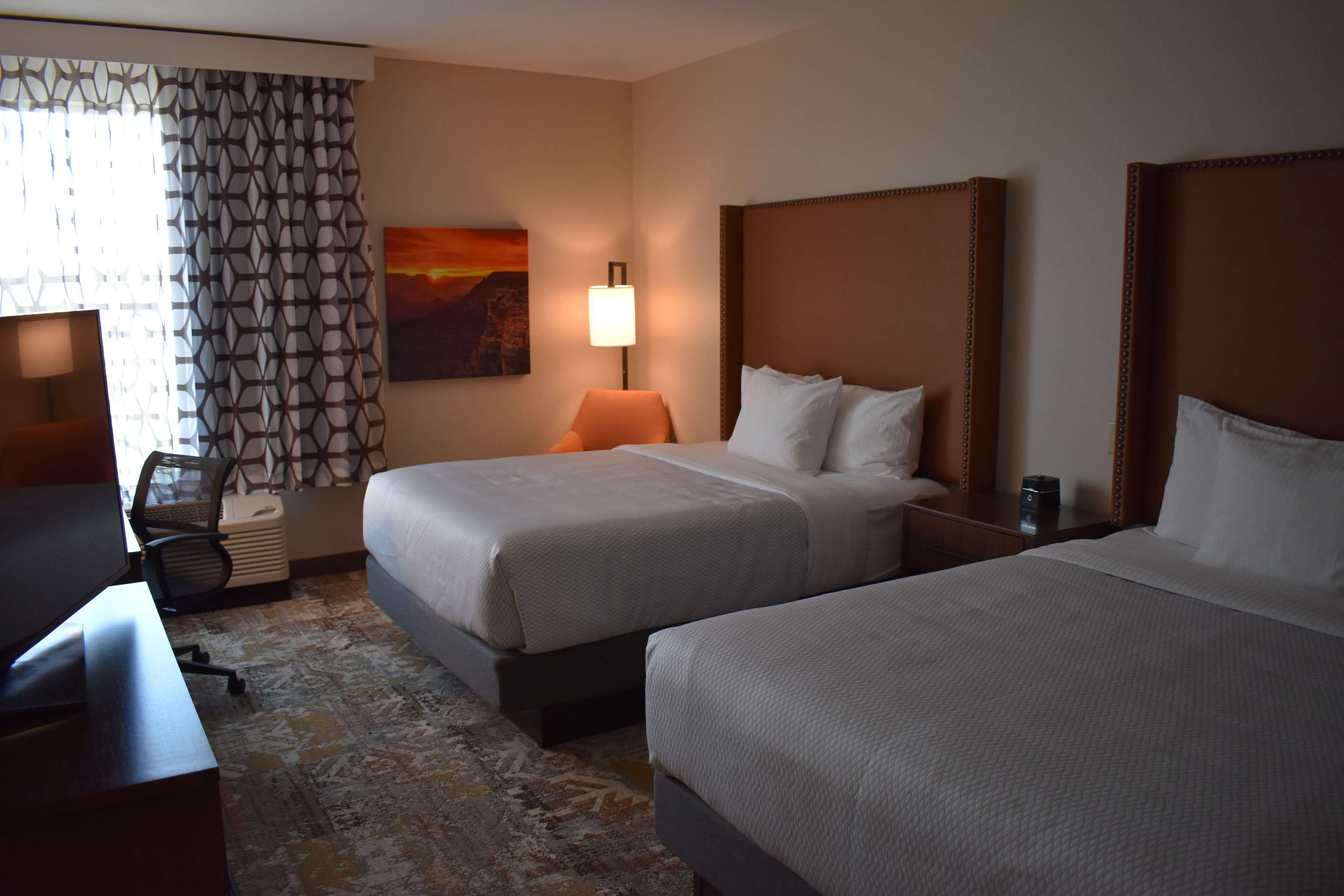 Une chambre d’hôtel avec deux lits, un bureau, une chaise, une lampe et un tableau au mur.