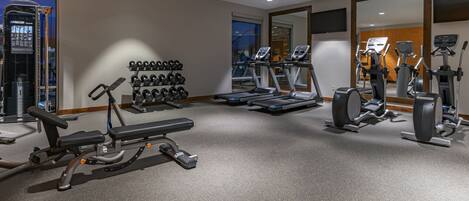A gym with treadmills, elliptical machines, free weights, and a mirrored wall.