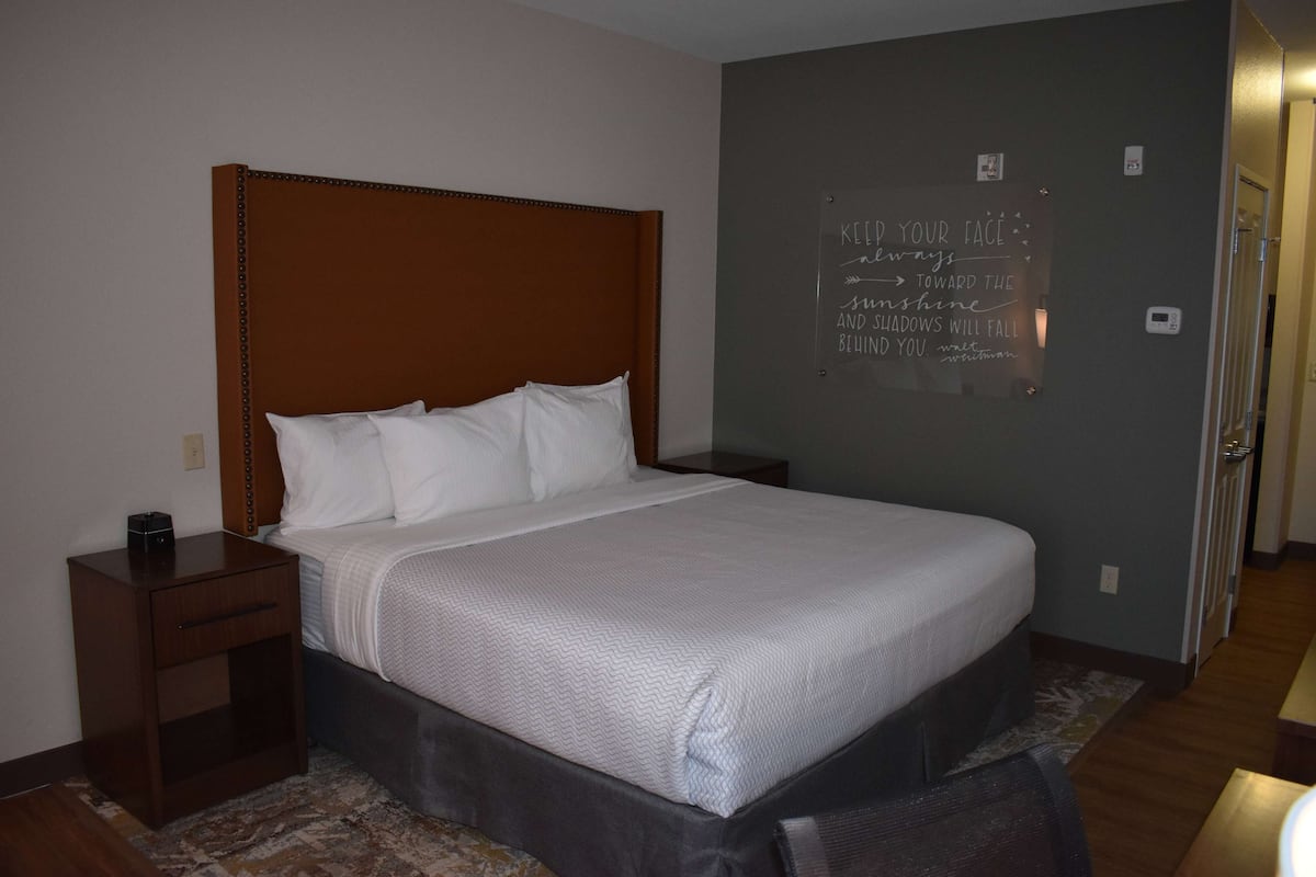 A neatly made bed with a wooden headboard, a bedside table with a lamp, and a motivational quote on the wall.