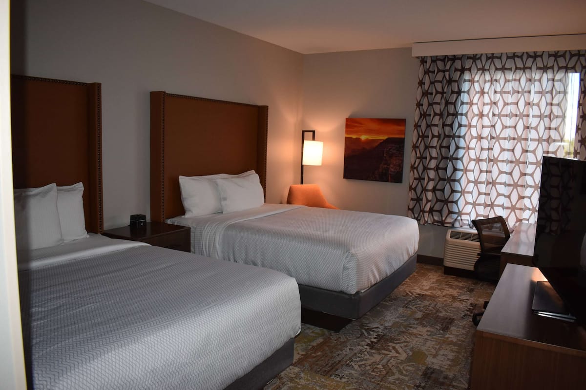 A hotel room with two beds, a desk, a lamp, a TV, and a patterned curtain.