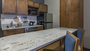 A kitchen with wooden cabinets, a stainless steel refrigerator, a microwave, and a granite countertop. - La Quinta Inn & Suites by Wyndham Flagstaff East I-40 (Flagstaff)
