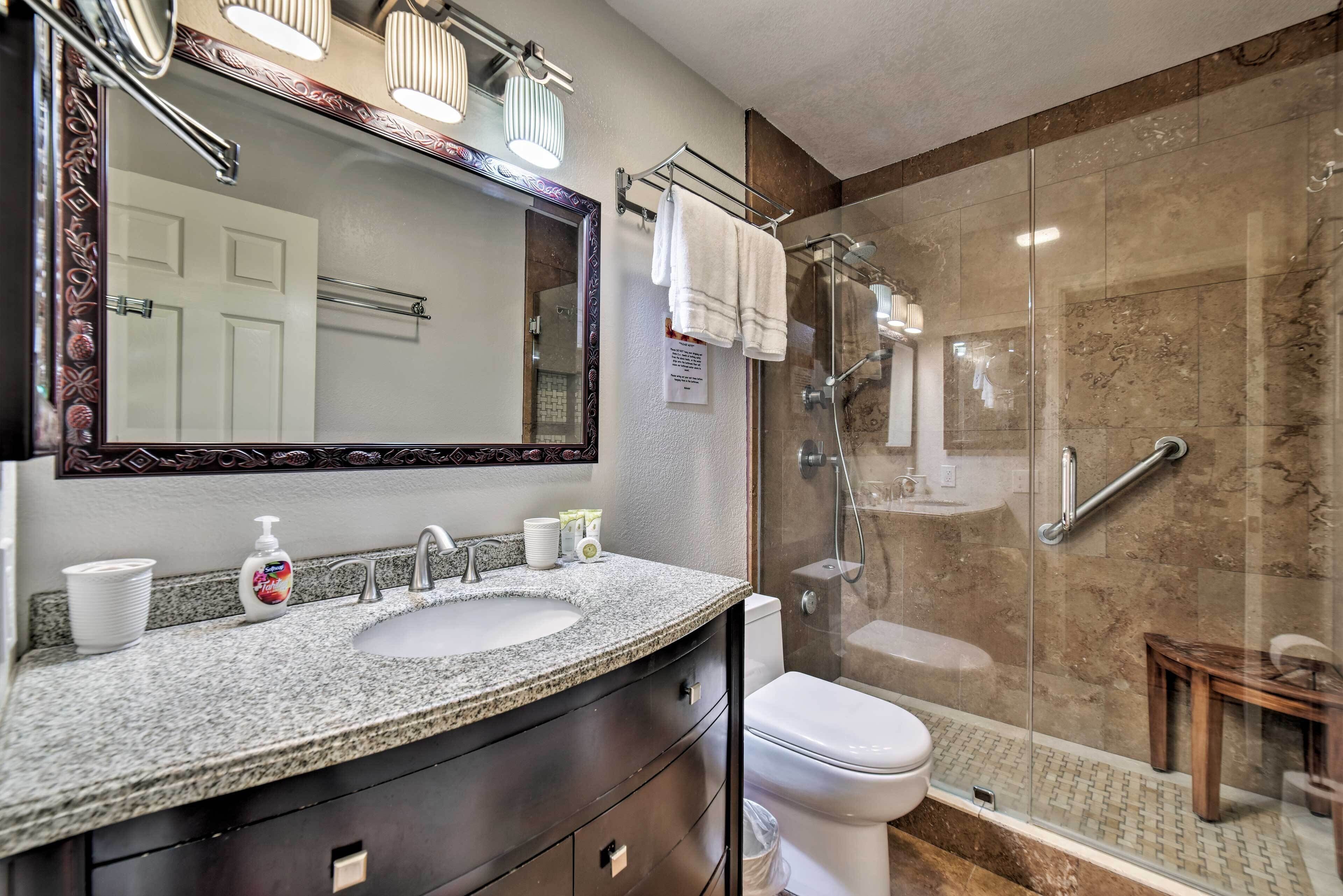 Une salle de bain dotée d’un lavabo avec un plan de travail en granit, d’un grand miroir, de toilettes et d’une douche à parois de verre.