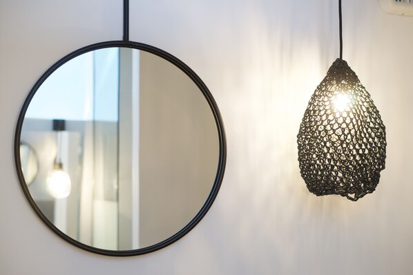 A round mirror with a black frame and a hanging pendant light with a woven design.