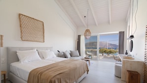 A spacious bedroom with a large bed, a small seating area, and a view of the outdoors. - Alancia Suites (Kefalonia)
