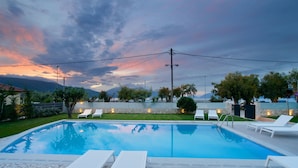 A swimming pool with lounge chairs, surrounded by a landscaped garden and a view of mountains. - Alancia Suites (Kefalonia)