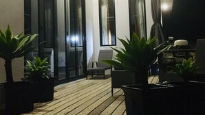 Um pátio moderno ao ar livre com piso de madeira, plantas em vasos e uma área de estar.